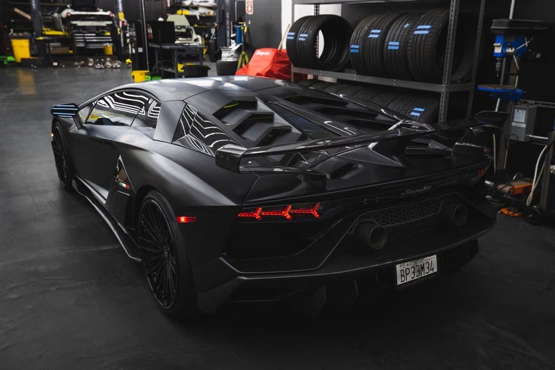 Rear three-quarter of a matte black Lamborghini Aventador SVJ in a workshop