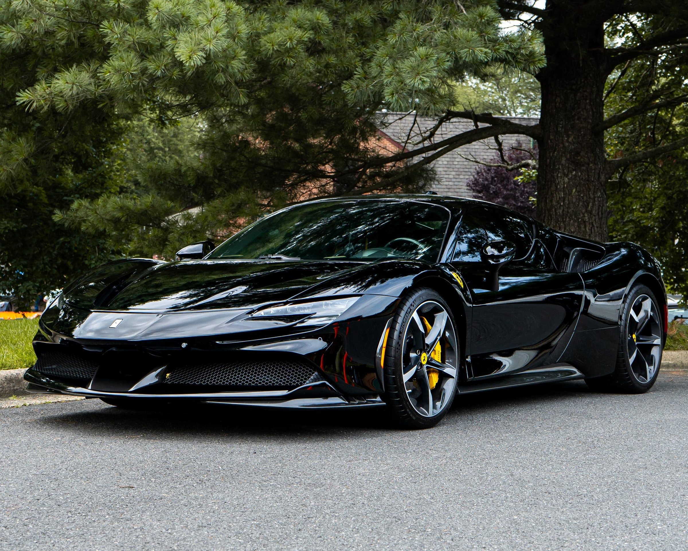 Black Ferrari SF90 parked in dappled daylight beneath pine trees